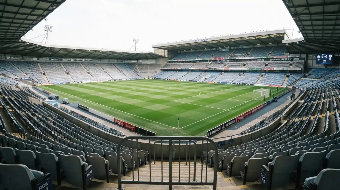 Ein leeres Fußballstadion bei Tageslicht von der Tribüne aus gesehen, der Rasen zeigt gleichmäßige Mähstreifen.